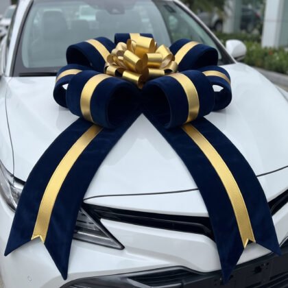 White car hood adorned with a large navy and gold ribbon bow, like a gift decoration in celebration